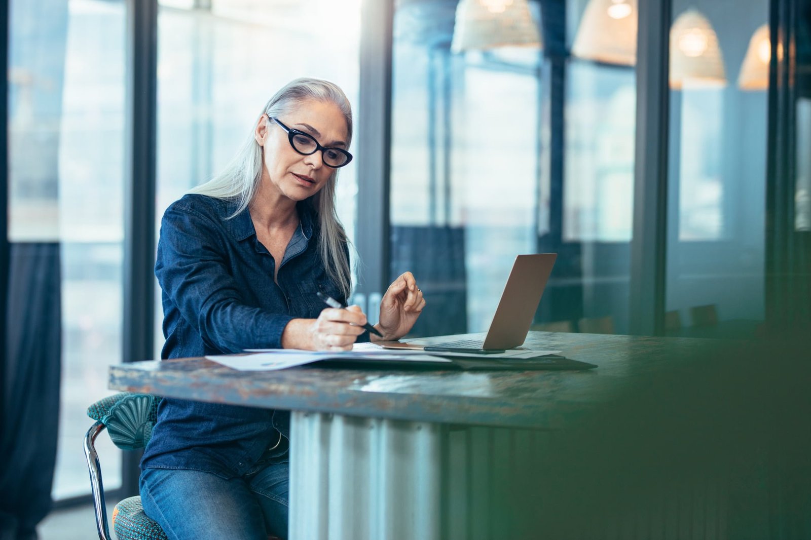 Portrait of senior woman sitting at table in office and reading few paper work. Business manager working on some documents at office.